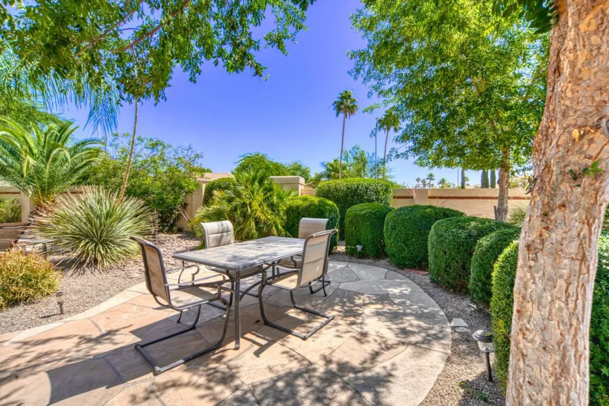 An exterior setting highlights an outdoor dining table with chairs surrounded by lush greenery and a pathway. The scene evokes tranquil, social moments such as outdoor meals, morning coffee, and garden parties.