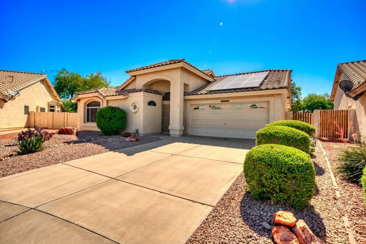 This exterior image features a welcoming front porch, a landscaped yard, solar panels on the roof, and a spacious driveway. The porch is clearly designed for socializing and enjoying the outdoors, with space for gatherings and relaxing evenings.