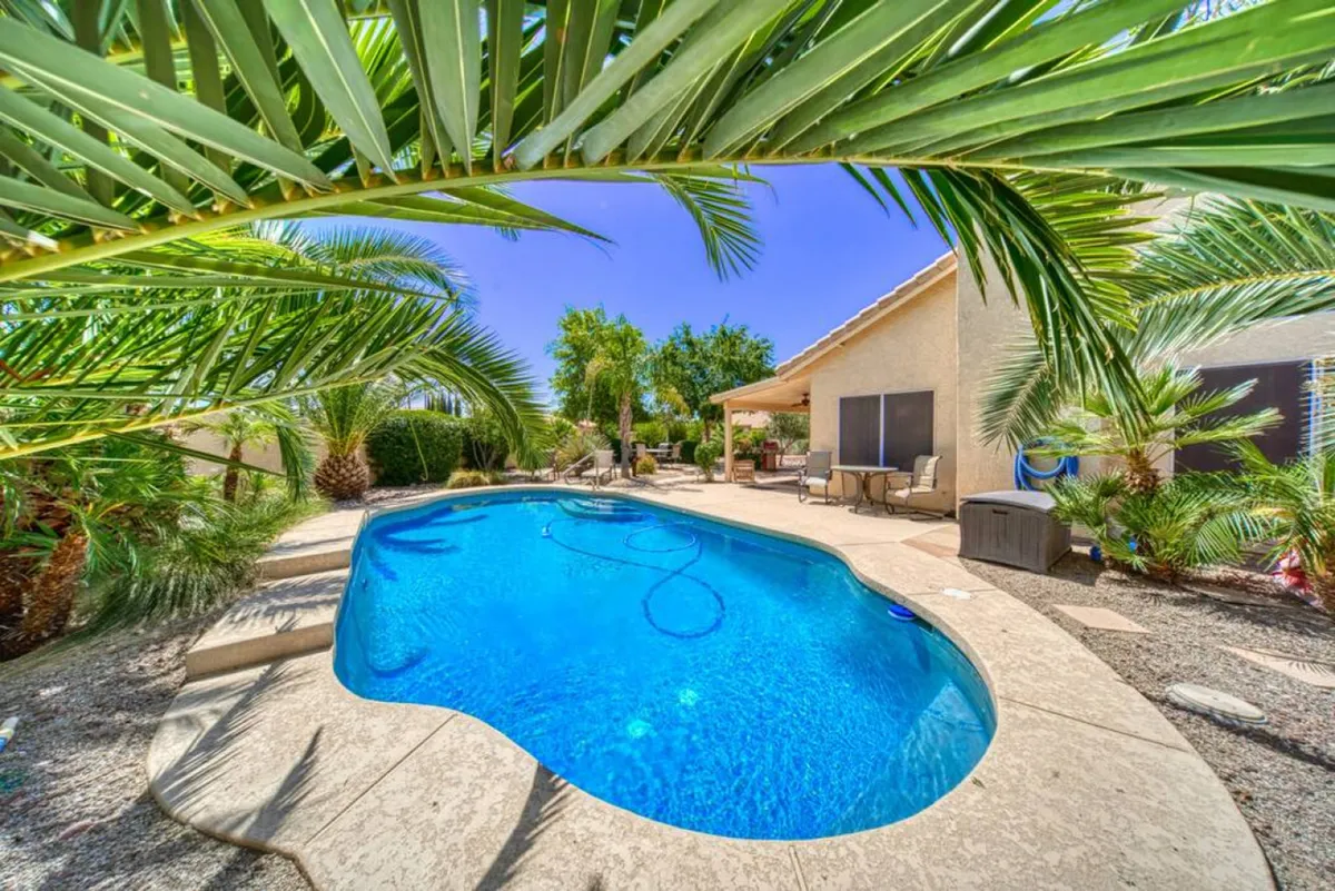 This image captures a sparkling swimming pool framed by lush palm trees, with an inviting outdoor seating area. Sunlight shimmers on the water, and the tranquil setting is complemented by comfortable lounge furniture—perfect for relaxation or socializing by the pool.