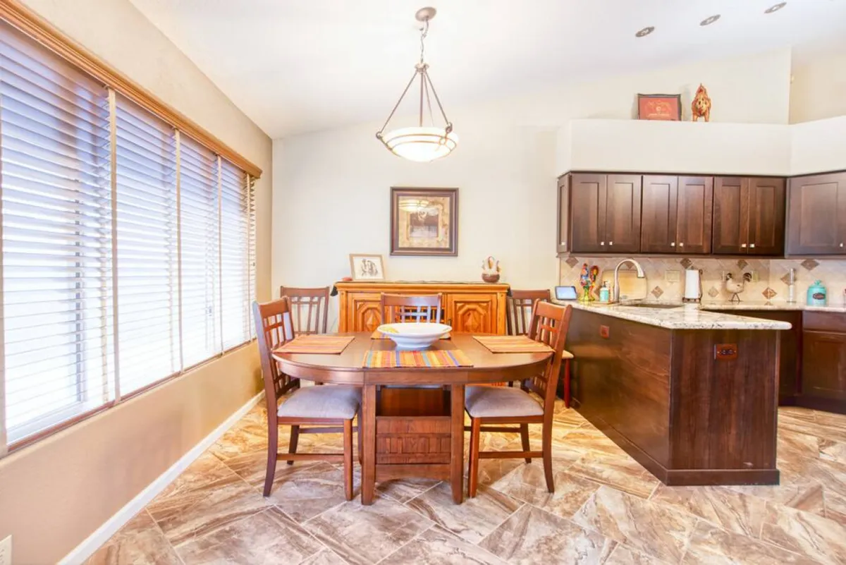 A large, wooden dining table with a colorful table runner is the focal point, surrounded by warm kitchen cabinetry and enhanced by framed artwork. The setting invites communal meals and casual or festive gatherings.