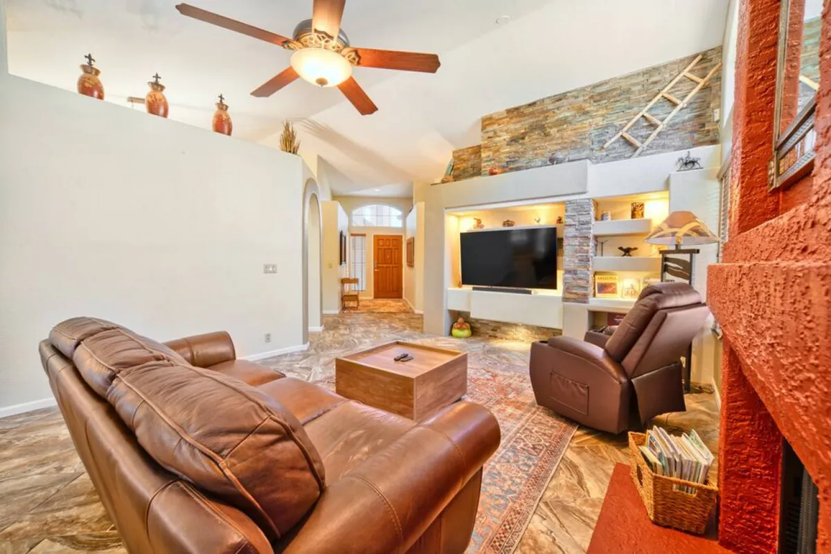 A modern living room featuring leather sofas, a stylish stone feature wall, an entertainment unit with a TV, and shelves adorned with books and decorative pieces. The arrangement encourages relaxation, movie nights, and intimate conversations.