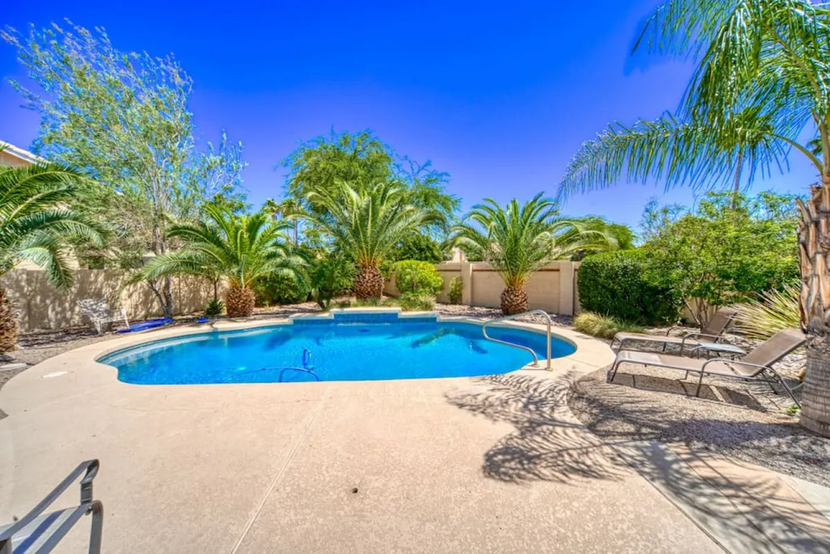 The image showcases a sparkling private swimming pool surrounded by swaying palm trees and inviting lounge chairs, set against the warm desert backdrop of Peoria, Arizona. The scene exudes relaxation and leisure, with ample space for sunbathing, swimming, and gathering with friends or family.