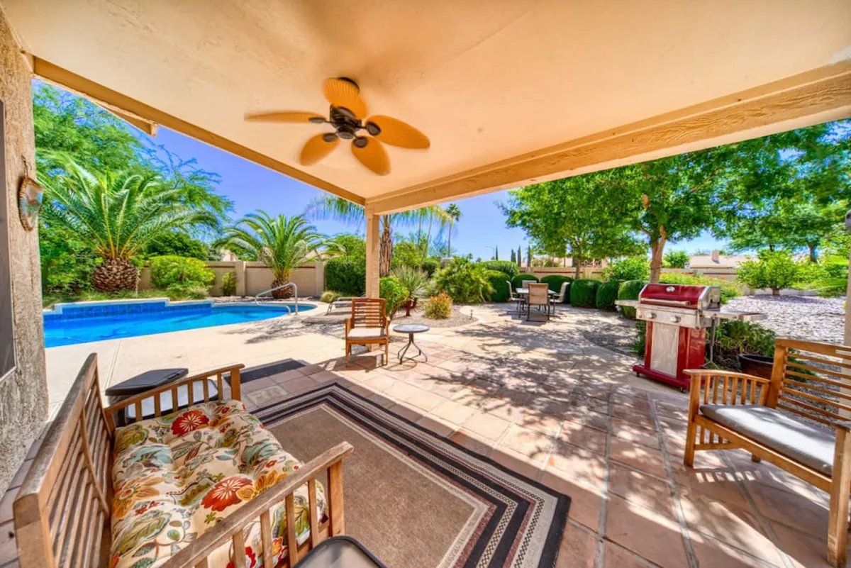A tranquil backyard scene featuring a private swimming pool glistening under the Arizona sun, surrounded by lush greenery. There is an inviting outdoor seating area with a grill, perfect for socializing or relaxing. The sunset glow enhances the serene atmosphere, and the space is clearly fenced, offering privacy and security.