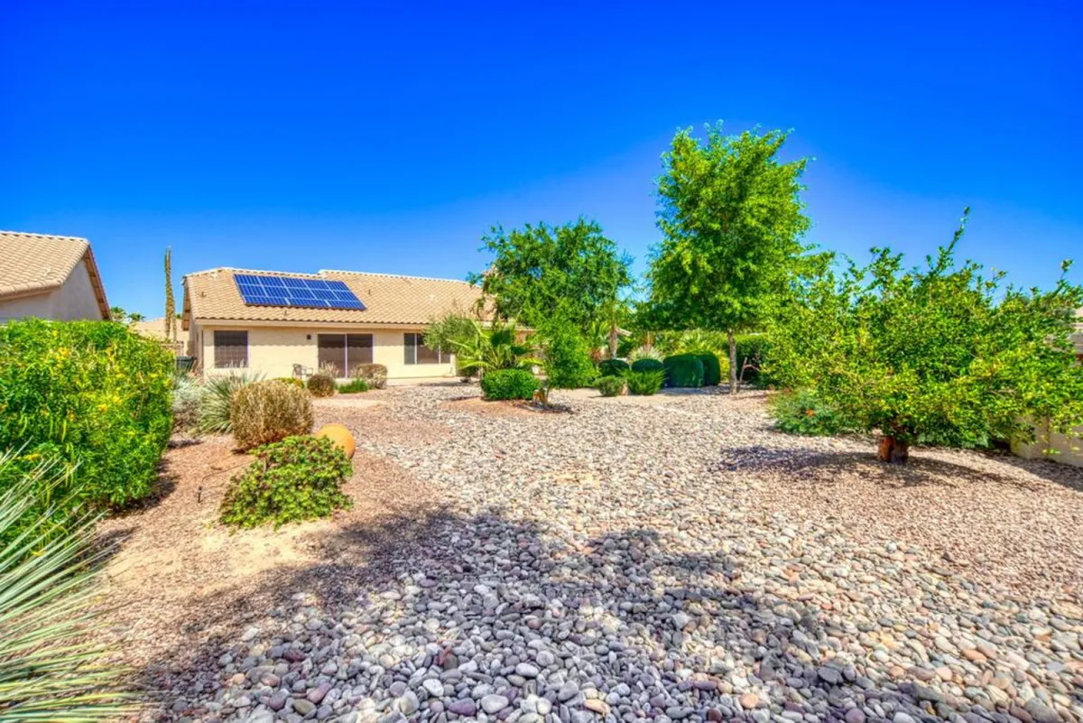 A tranquil exterior scene showing a house with solar panels, surrounded by lush greenery and a gravel landscape. The image exudes peace and connection to nature—perfect for enjoying sunny afternoons outside or stargazing at night.