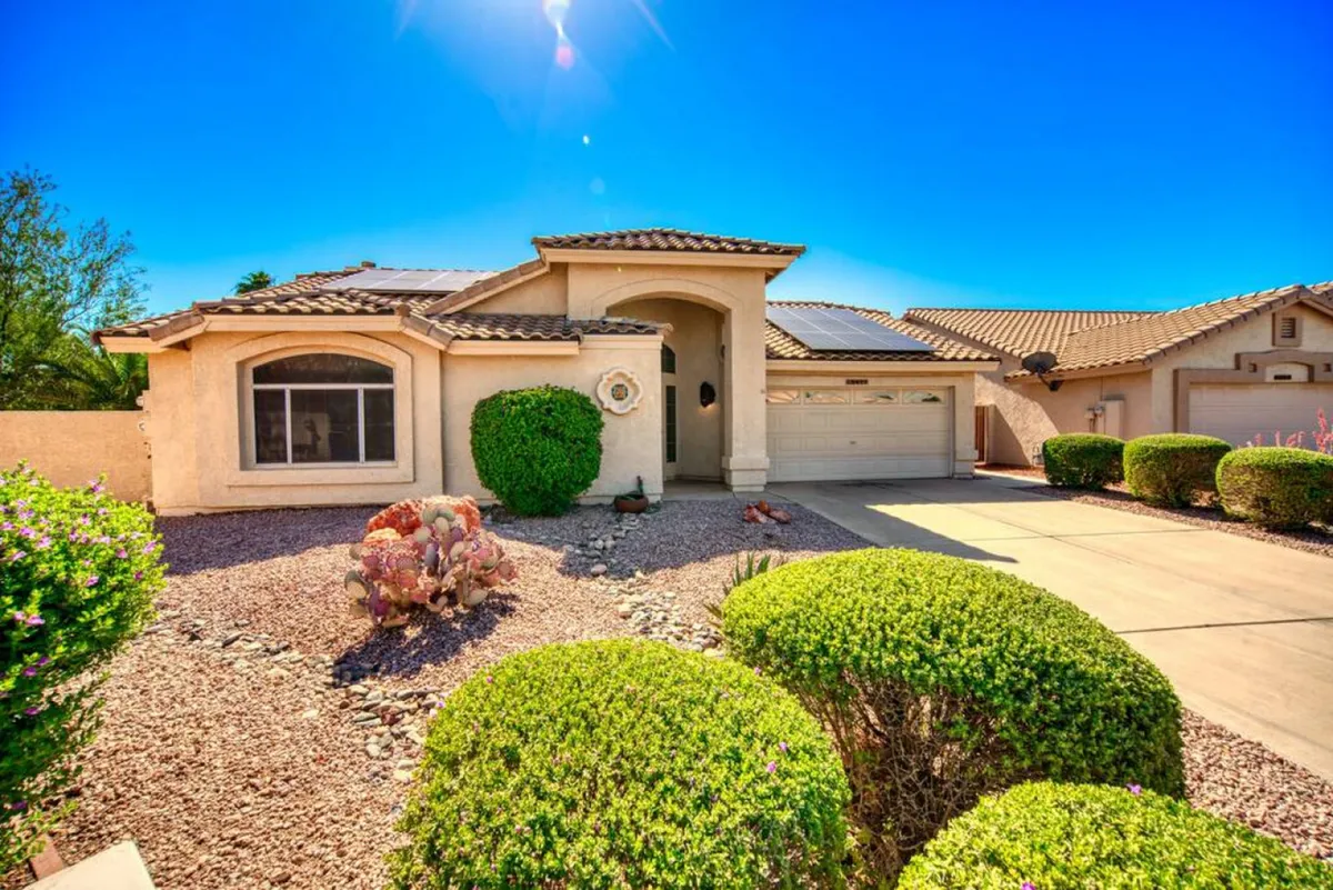 A beautifully maintained front yard with lush bushes and a view of the house facade and driveway, all set in an inviting neighborhood. The outdoor space feels open and welcoming, ideal for appreciating sunny Arizona days.