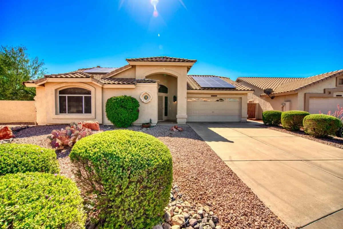 A view of the home's front entrance framed by a well-maintained landscaped yard and a spacious driveway. The inviting exterior hints at gatherings and outdoor social life, while the green space suggests relaxation and time spent outside.