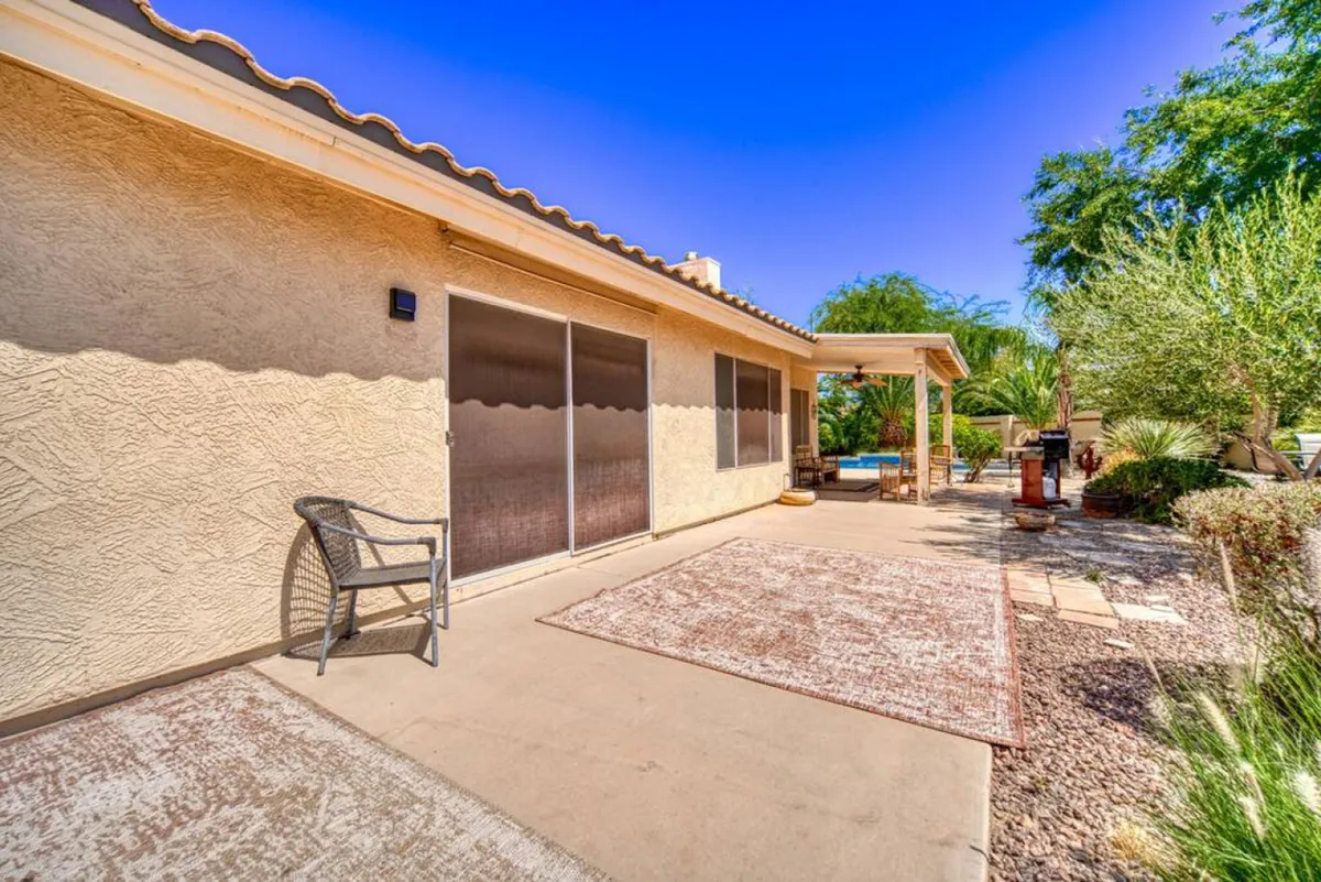 A welcoming patio area with comfortable outdoor seating and a rug, positioned under a shaded structure. The pool is visible in the background, tying the patio and pool spaces together, while the tranquil setup invites relaxation and gatherings with friends or family.