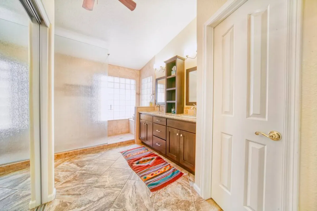 A serene, modern bathroom is depicted with a double sink vanity, a colorful rug, and large windows that allow natural light to pour in. The atmosphere is calming and fresh, with modern fixtures that give a spa-like feel.