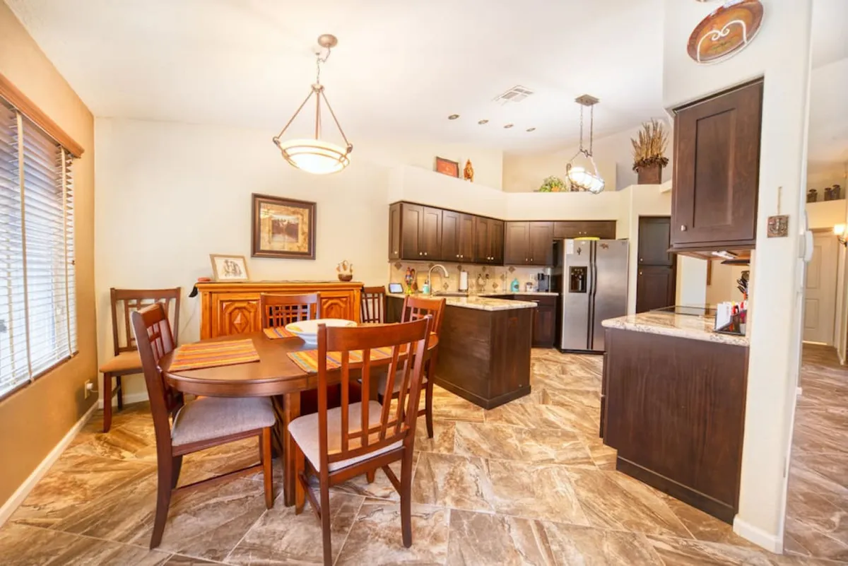 A warm and inviting dining area adjacent to the kitchen, featuring a generously sized dining table, stylish kitchen cabinets, and carefully curated decorative items on open shelves. The soft lighting and thoughtful arrangement create an intimate yet functional setting for meals and gatherings.