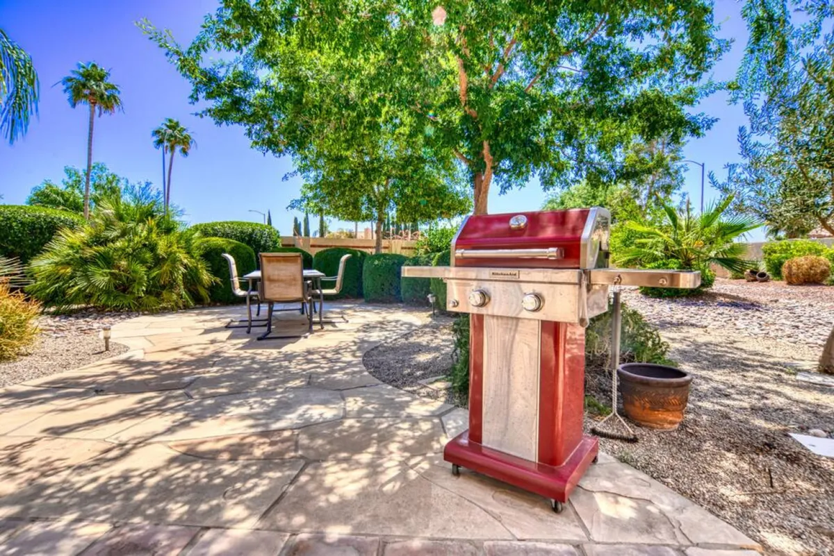 A lively exterior scene featuring a grill, outdoor seating, and abundant greenery. The setup is ideal for barbecuing, al fresco dining, and relaxed outdoor gatherings, capturing the spirit of communal celebrations and casual get-togethers.