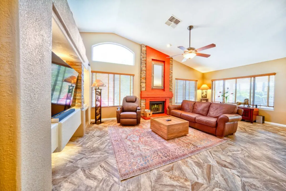 A spacious living area with a leather sofa, soft area rug, a prominent fireplace, and large windows letting in natural light. The space is designed for reading, watching TV, and hosting lively gatherings, exuding warmth and comfort.