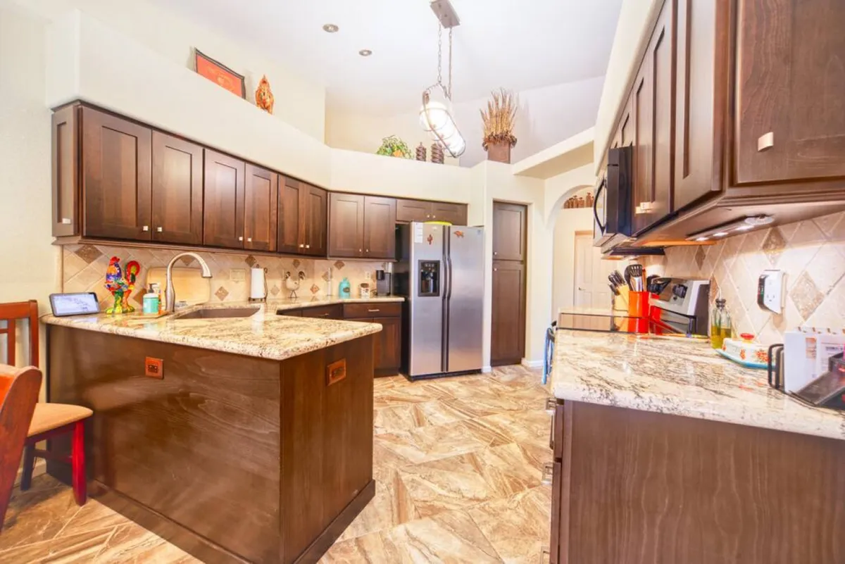 A modern kitchen featuring expansive granite countertops, sleek dark wood cabinetry, and state-of-the-art stainless steel appliances. Decorative elements on the shelves add personality, while the open layout suggests ample space for cooking, baking, and entertaining.