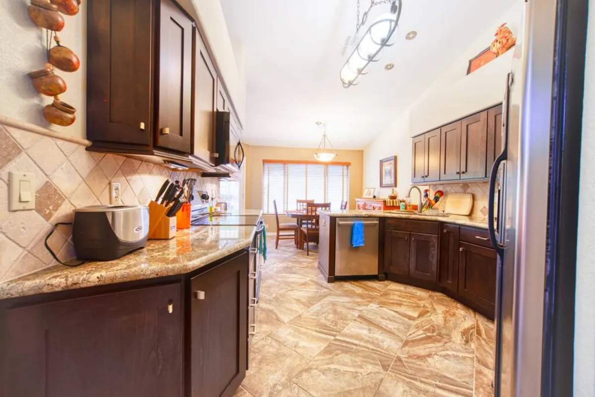An open-plan kitchen and dining space, equipped with granite countertops, dark wooden cabinets, a modern dining table, and updated kitchen appliances. The layout invites both everyday meals and special gatherings, reflecting a balance of style and practicality.